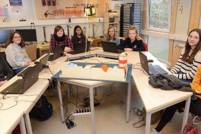 Eine Gruppe von Schüllerinnen sitzt U-förmig um ein Hafenmodell, vor ihnen auf den Tischen stehen Laptops.