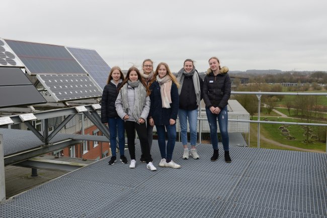 Eine Gruppe Schülerinnen posiert vor Solarzellen auf einem Dach. Im Hintergrund der Blick über den Campus.