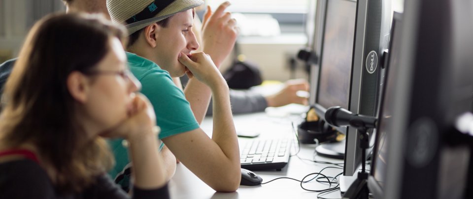 Studierende sitzen nebeneinander in einer Reihe im PC-Labor und arbeiten je an einem Rechner.