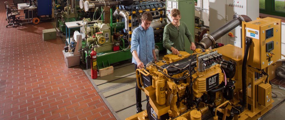 Zwei Studenten in der Maschinenhalle arbeiten an einer Baumaschine.