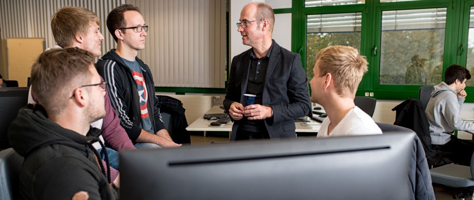 Professor und Studierende im Gespräch in einem Computerlabor.