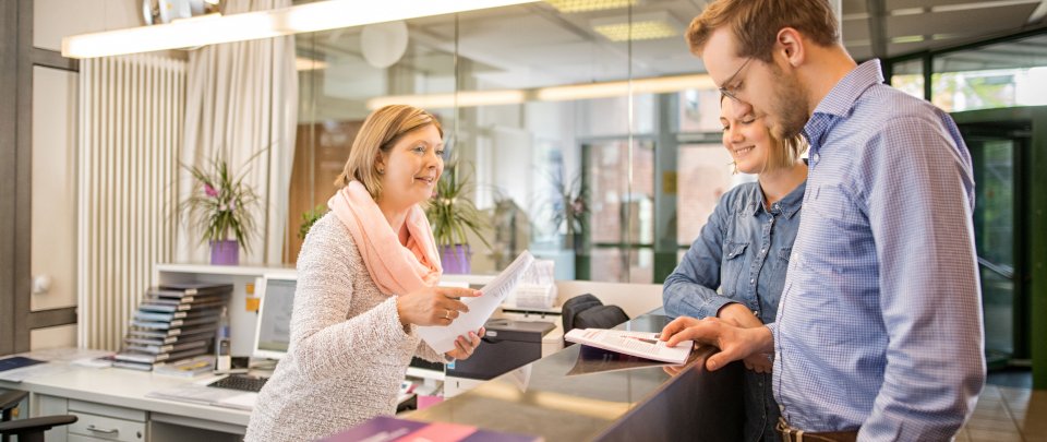 Eine Mitarbeiterin berät am Info Point der Hochschule zwei Studierende.