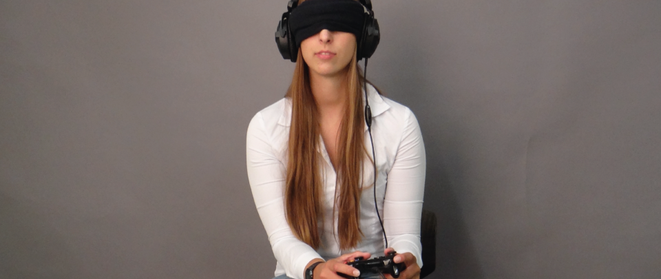 Person mit verbundenen Augen hat einen Kopfhörer auf dem Kopf und einen Game Controller in der Hand