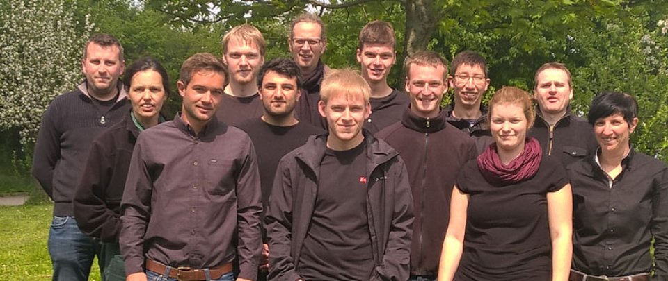 Eine Gruppe Studierender und Lehrender posieren auf einer Wiese. Alle tragen dunkle Oberteile.