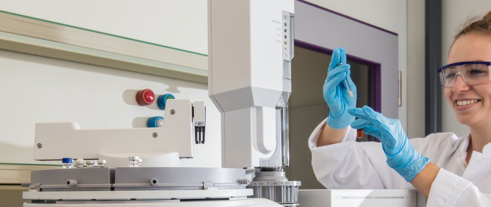 Studierende in Laborkittel hält eine Pipette in den Händen. Vor ihr ist Laboraapartur zu erkennen.