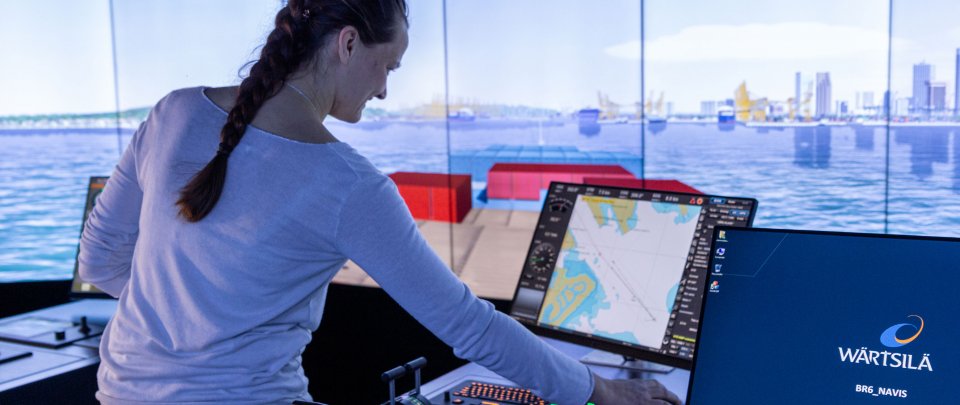 Frau mit Zopf in Schiffsimulator guckt auf Monitor mit aktueller Seekarte