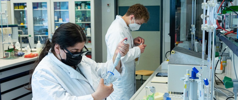 2 Personen in einem Labor mit Schutzmasken und weißer Kleidung benutzen Pipetten
