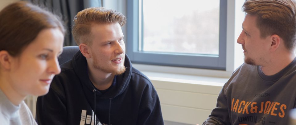 Drei Studierende: Zwei sprechen miteinander, eine schaut auf etwas anderes. 