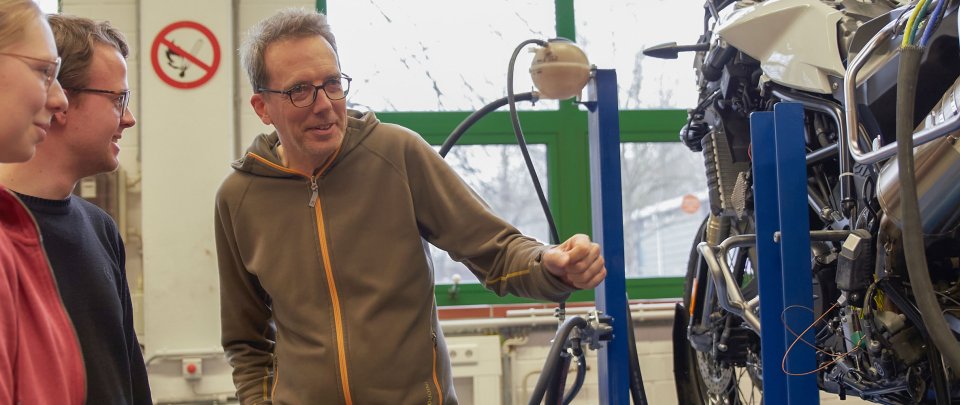 Studierende und Dozent stehen neben einem Motorrad.