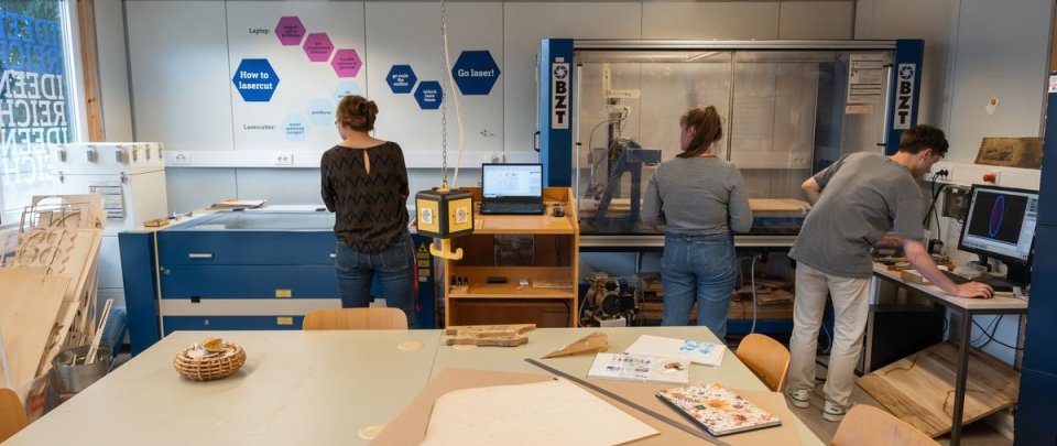 Studierende im ideenreich. Im Bildvordergrund ein Arbeitstisch mit Kabeln, Werkzeugen und 3D-Druck-Produkten.