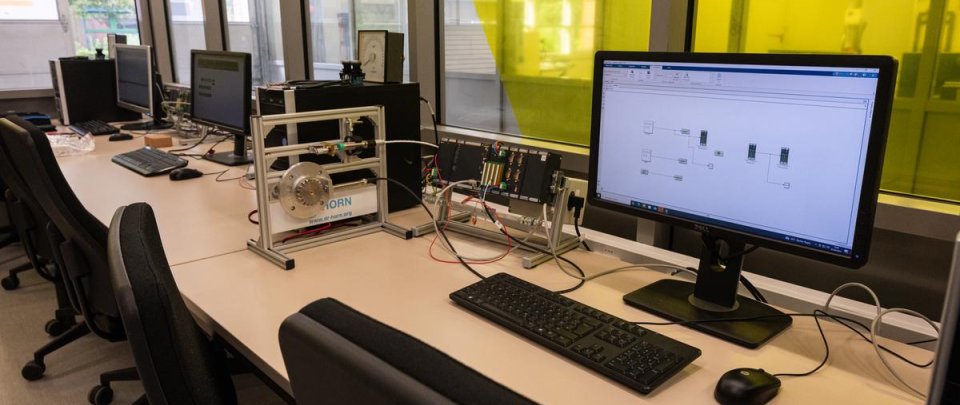 Mehrere Computerarbeitsplätze mit angeschalteten Monitoren und verschiedenen elektrischen Messvorrichtungen auf den Schreibtischen.