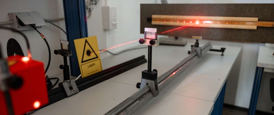 Versuchsaufbau mit einem Laserstrahl, der auf eine Messlatte zeigt.