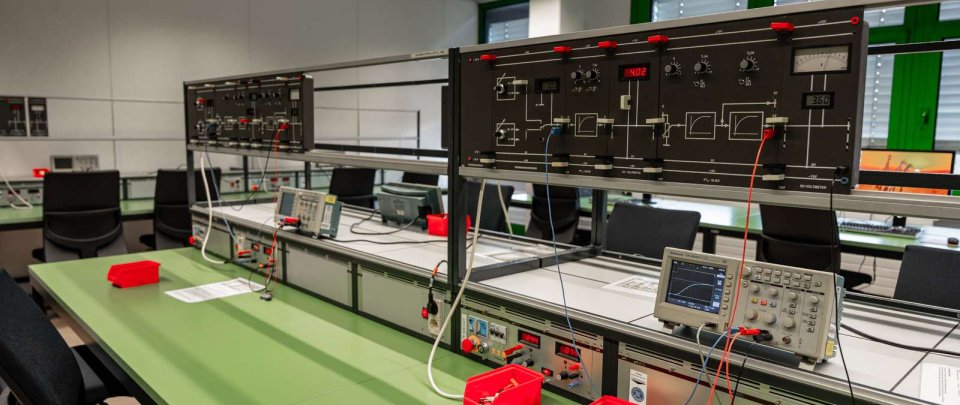 Auf dem Bild sind im Labor verschiedene Laborgeräte und sonstige Ausstattung zu sehen, wie zum Beispiel Monitore, Oszilloskope und Messgeräte.