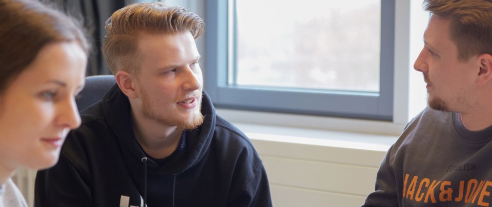 Drei Studierende sitzen zusammen, angedeutet ist ein Bildschirm zu sehen.
