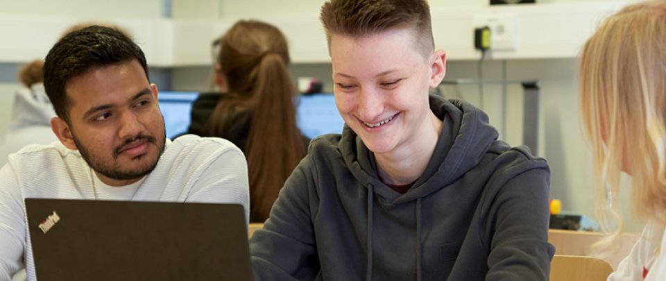 Drei Studierende sitzen in einem Labor an einem Tisch und arbeiten gemeinsam am Laptop.