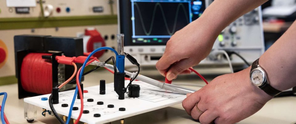 Nahaufnahme eines Arbeitsplatzes im Elektrotechnik-Labor mit zwei Händen, die gerade eine Schaltung umstecken.