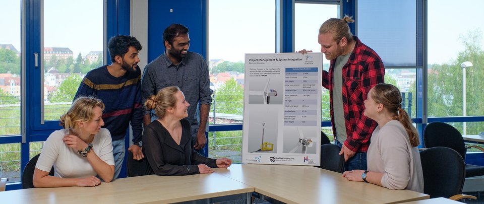 Eine Gruppe von Studierenden sitzt in einem Seminarraum und schaut sich gemeinsam ein Plakat zum Thema Windenergie an.