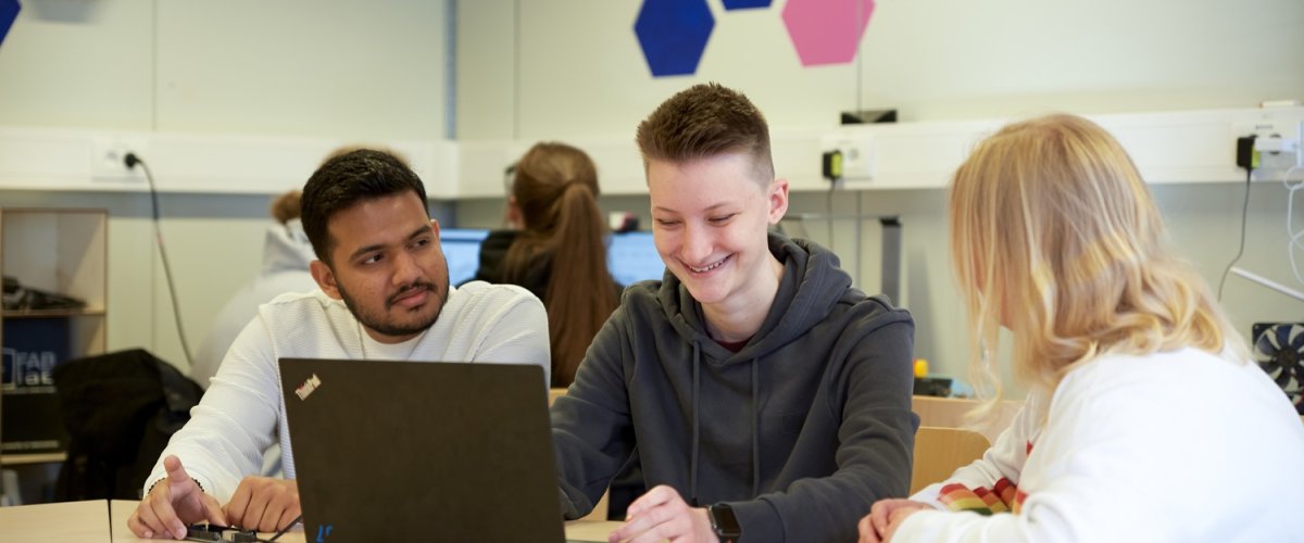 Drei Studierende sitzen in einem Labor an einem Tisch und arbeiten gemeinsam am Laptop.