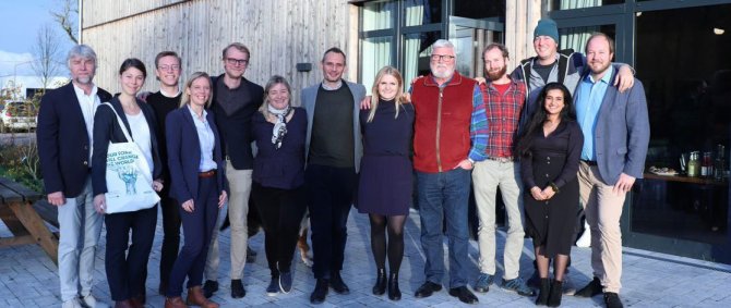 Gruppe von Menschen steht an einem sonnigen Tag vor einem Gebäude und lächelt für die Kamera.