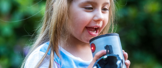 Kind hält ein Gerät in der Hand, in das es hineinspricht.