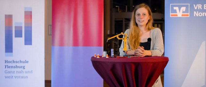 Junge Frau steht an einem Stehtisch, darauf ein Spielzeigkran. Hinter ihr Werbeaufsteller.