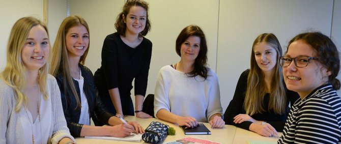 Sechs Studentinnen sitzen im Halbkreis um einen Tisch und lächeln in die Kamera