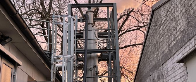 Scrubber vor abendlichem Himmel. Eien Art Schornstein wird von einem Gerüst umfasst, der Himmel dahinter ist orange-rötlich gefärbt.