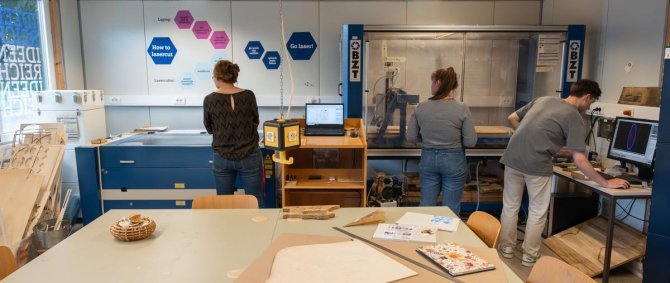 Studierende im ideenreich. Im Bildvordergrund ein Arbeitstisch mit Kabeln, Werkzeugen und 3D-Druck-Produkten.