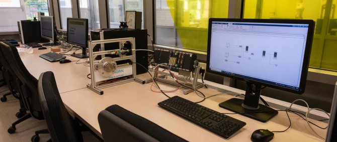 Mehrere Computerarbeitsplätze mit angeschalteten Monitoren und verschiedenen elektrischen Messvorrichtungen auf den Schreibtischen.