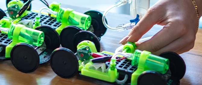 Nahaufnahme von drei grünen Rennautos, die gerade mit einer Pipette mit Wasserstoff befüllt werden.