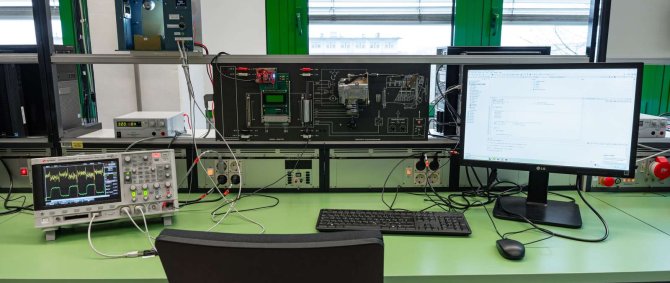 Im Raum befinden sich verschiedene Geräte, Monitore und Laborausstattung. Es handelt sich um ein Regelungstechnik-Labor, das für praktische Experimente genutzt wird.