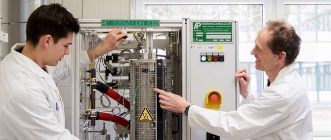 Ein junger und ein Mann mittleren Alters stehen in einem Laborraum, beide tragen Laborkittel.