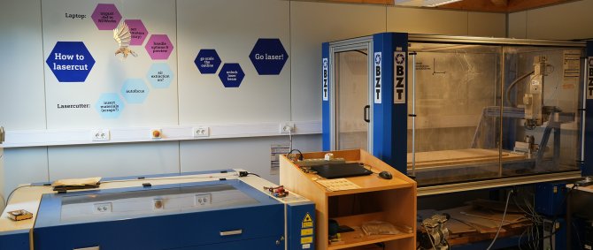 In einem Raum stehen ein Lasercutter und eine CNC-Fräse, an der Wand sind bunte Rauten.