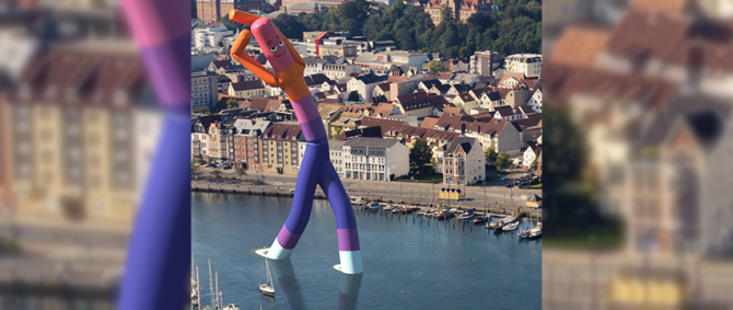 Der Flensburger Hafen aus der Vogelperspektive - im Wasser steht ein riesiges Windmännchen in den Farben der Hochschule Flensburg.