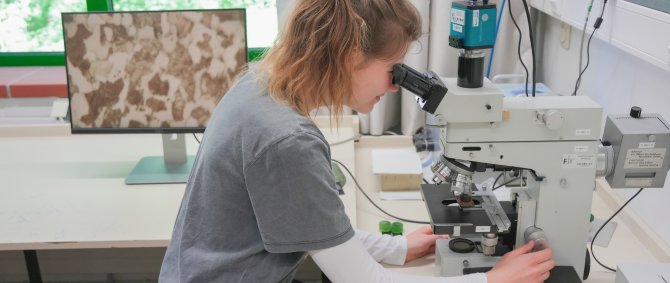 Eine Studentin blickt im Labor für Werkstofftechnik durch ein Mikroskop.