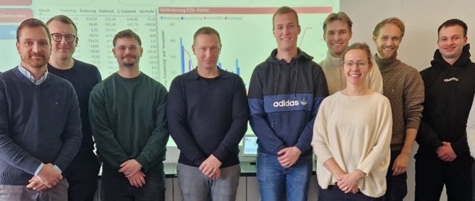 Eine Gruppe von Studierenden steht mit Vertretern der NVB und Sina Völtzer in einem Seminarraum vor einem Dashboard und lächelt in die Kamera.