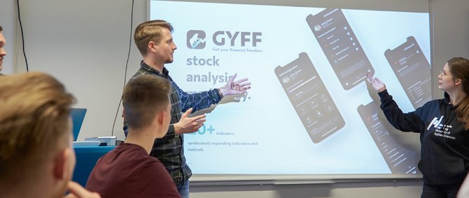 Studierende erklären etwas an einem Bildschirm, andere hören zu.