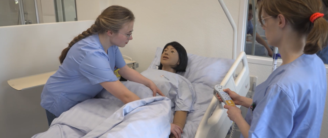 Zwei Pflegestudentinnen üben an einer lebensechten Puppe im Flensburger HealthLab eine Pflegesituation.
