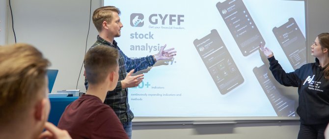 Studierende erklären etwas an einem Bildschirm, andere hören zu.
