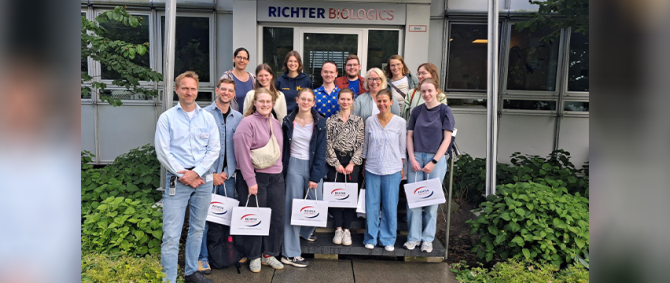 Eine Gruppe von Studierenden und Lehrenden steht lächelnd vor einem Hauseingang, über dem groß "Richter Biologics" steht.
