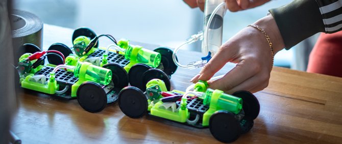 Nahaufnahme von kleinen Rennautos und einem Paar Hände, die diese mit einer Spritze betanken.