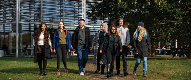 Eine Gruppe junger Menschen läuft gemeinsam über den Campus. Im Hintergrund ein Gebäude, Wiese und ein Baum.