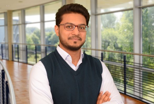 Porträtfoto: Muhammad Tariq im audimax. Er trägt kurze Haare und Bart und eine Brille. Er trägt einen Pullunder über einem weißen Hemd.
