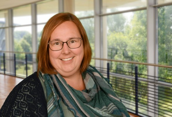 Porträtfoto: Jolyn Muijsers im audimax, sie trägt die braunen Haare offen, ein Brille und ein bunt gemustertes Tuch über dem  dunklen Oberteil.