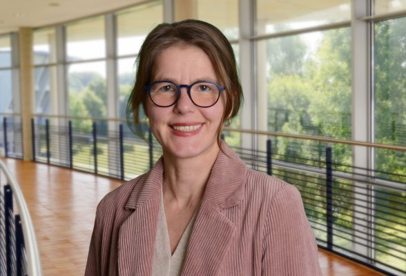 Porträtfoto: Sabine Uhl im audimax, sie trägt Brille und die Harre locker zusammengebunden. Über einem hellen Oberteil trägt sie ein alt-rosa Cord-Jackett.