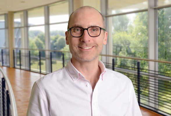 Porträtfoto: Sven Bertel im audimax, er trägt eine Brille, die Haare sehr kurz und einen Dreitagebart. An seinem hellen Hemd ist der oberste Knopf geöffnet.