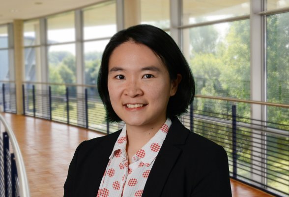 Porträtfoto: Wei-Hsin Tsao im audimax, sie trägt die dunklen Haare kinnlang und offen und einén dunklen Blazer über einem weißen Oberteil mit rotem Muster.