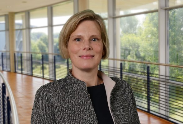 Porträtfoto: Sabine Wienke Seeger im audimax, sie trägt kurze, blonde Haare und eine schwarz-weiß gemusterte Jacke über einem schwarzen Oberteil.