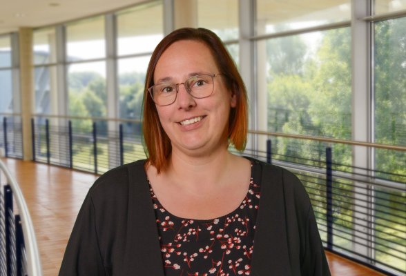 Porträtfoto: Jolyn Muijsers im audimax, sie trägt die kinnlangen, rötlich braunen Haare offen, ein Brille und eine dunkle Jacke über dem gemusterten Oberteil.