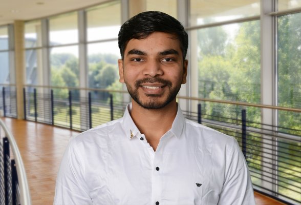 Porträtfoto: Ajudiya Kishan im audimax, er trägt dunkle, kurze Haaare und Bart und ein weißes Hemd.